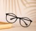 A stylish pair of black eyeglasses placed on a white surface with artistic shadows in the background.