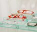 Stylish red eyeglasses displayed on a glass shelf in an eyewear store.